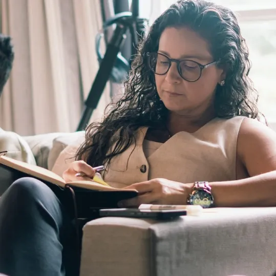 Camila Gracioli sentada em um sofá, lendo anotações com atenção.